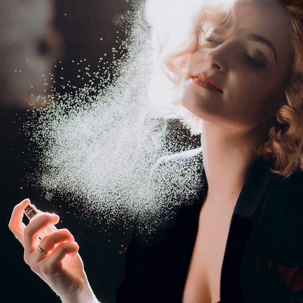 Frau sprüht sich Parfum aufs Dekolleté